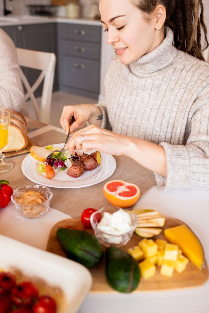 about-us-02 A woman in a cozy sweater enjoys a healthy breakfast with fruit and salad indoors.